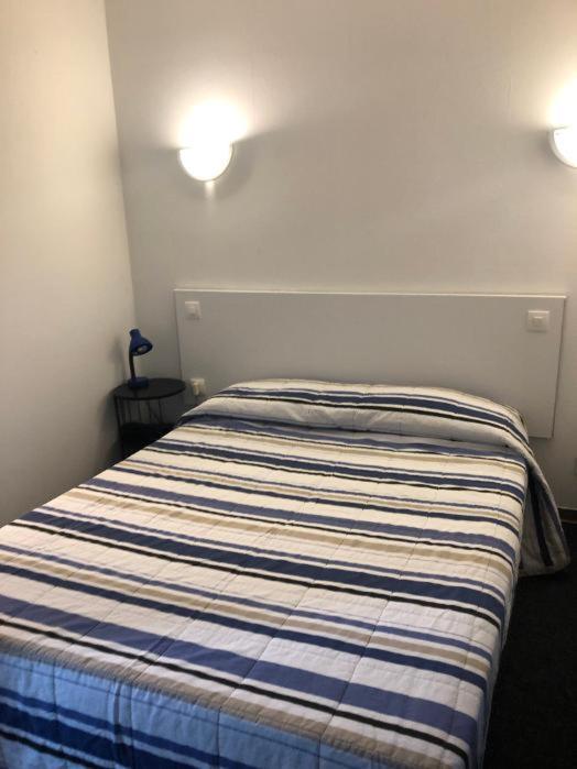 a bed in a bedroom with two lights on the wall at Hôtel Le Relais in Fleurance