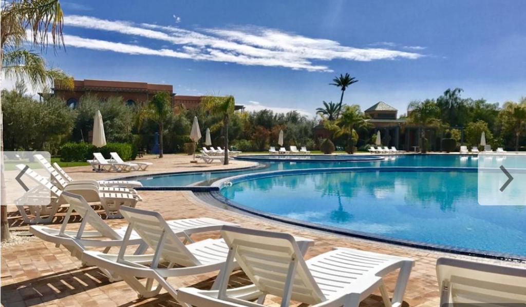 馬拉喀什的住宿－marrakech palmeraie village Etablissement jasmin，度假村旁的游泳池,带白色椅子