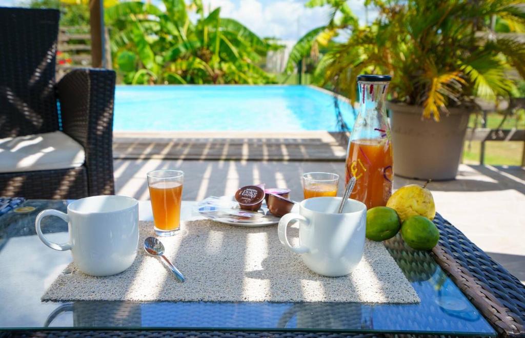 una mesa con bebidas y fruta junto a una piscina en La Villa Soleil :), en Sainte-Anne