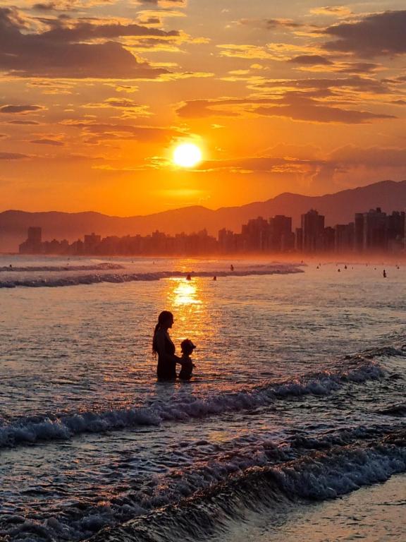 a woman and child playing in the water at the beach at sunset at Apartamento Classe A in Praia Grande