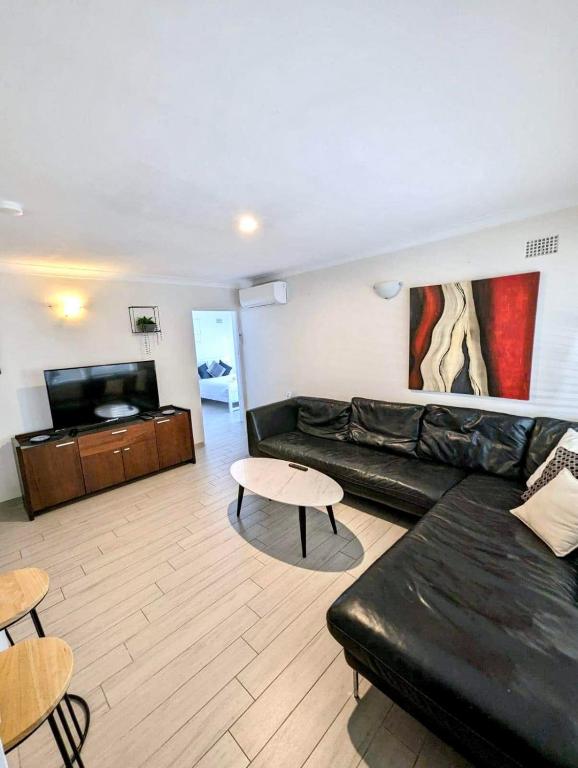 a living room with a black leather couch and a tv at Lotus Stay Manly - Apartment 31H in Sydney