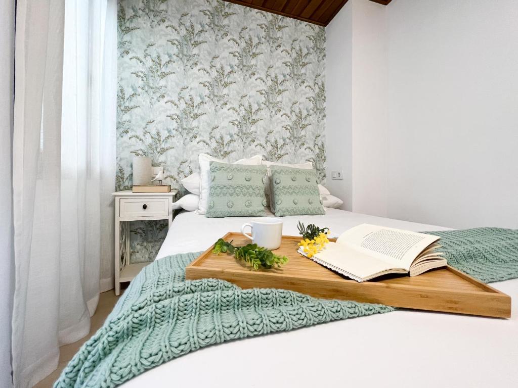 Una cama con una bandeja de madera con un libro y flores. en Con Alma, en Plasencia