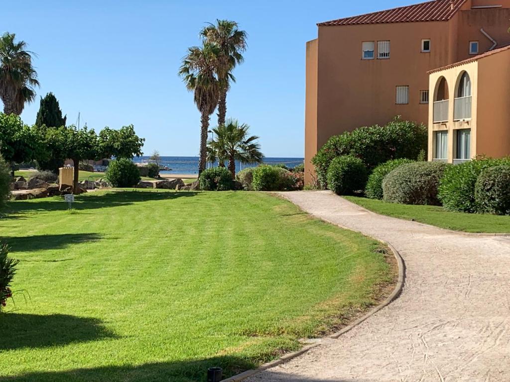 un chemin menant à un bâtiment avec des palmiers et l'océan dans l'établissement Appartement Bord de mer, à La Londe-les-Maures