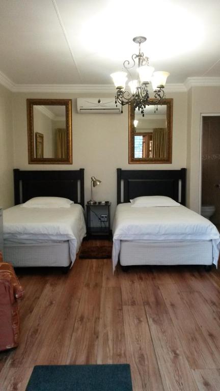 two beds in a room with wooden floors and mirrors at VAAL RIVER GUEST HOUSE in Vanderbijlpark