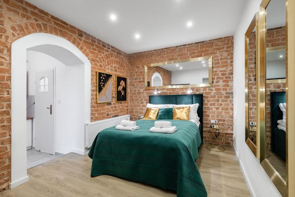 a bedroom with a green bed with a brick wall at Apartamenty K&B Toruń in Toruń