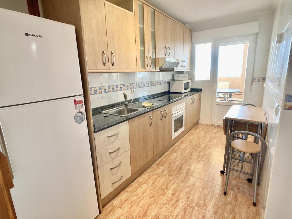 a kitchen with a white refrigerator and a table at Spanish Connection - Los Miradores del Puerto in La Manga del Mar Menor
