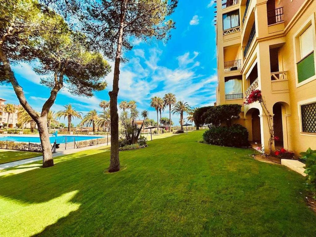 une pelouse en face d'un bâtiment avec piscine dans l'établissement Residencial Alcaraván, Isla Canela - By AC REAL, à Isla Canela