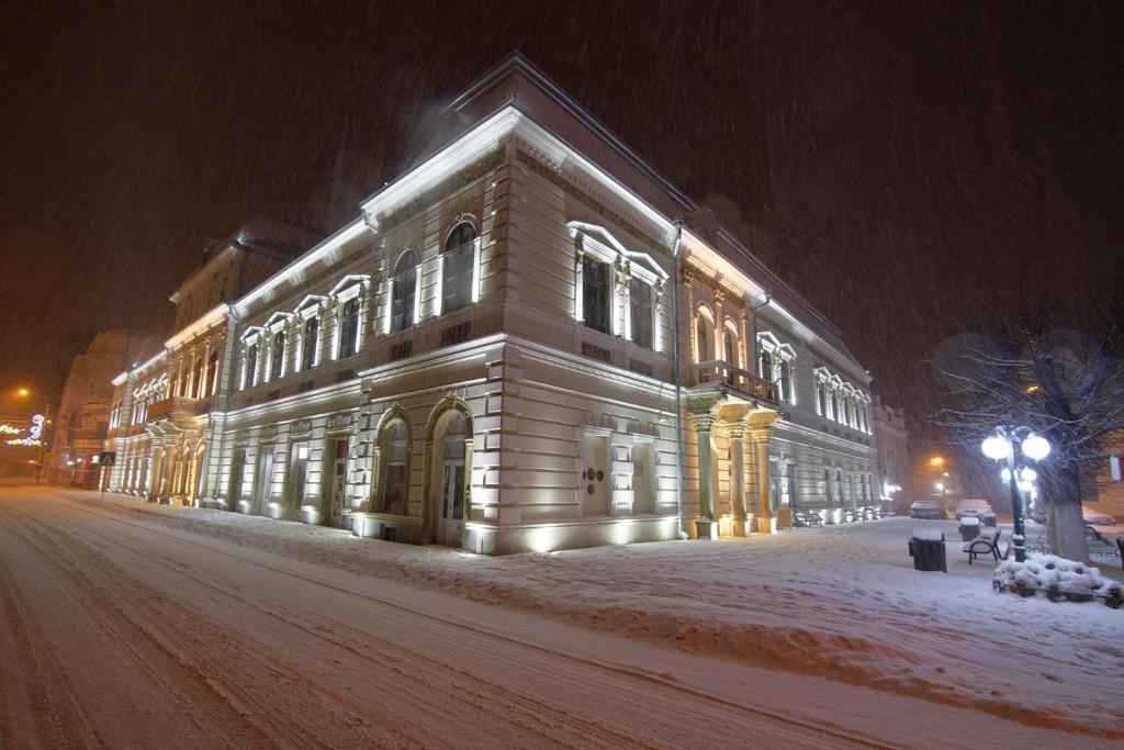 a lit up building on a snowy street at night at Buchenland Hotel in Câmpulung Moldovenesc