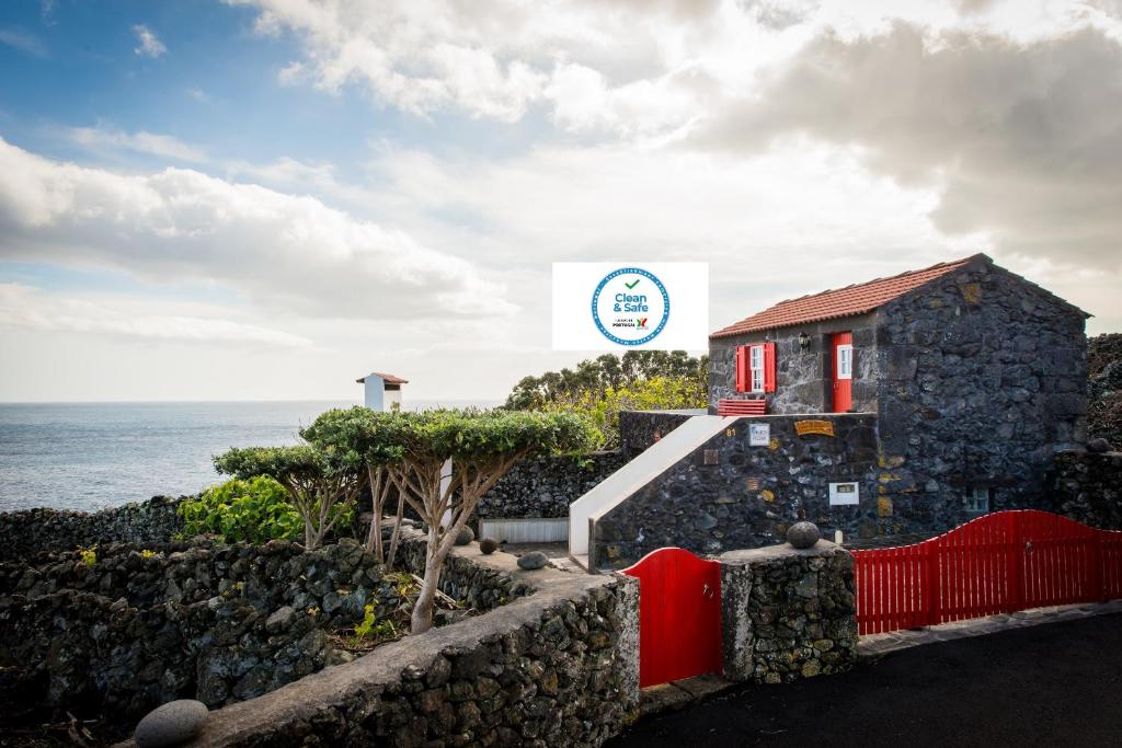 a building with a red fence next to the ocean at Adega Velha in Calheta de Nesquim