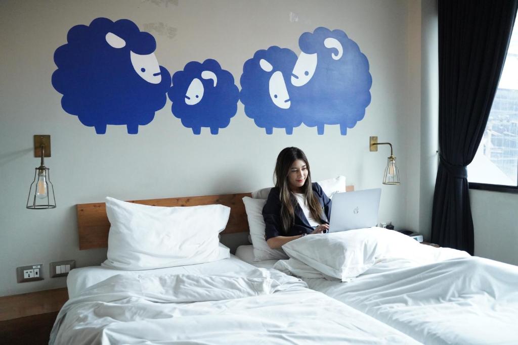 a woman sitting on a bed with a laptop at Kokotel Bangkok Surawong in Bangkok