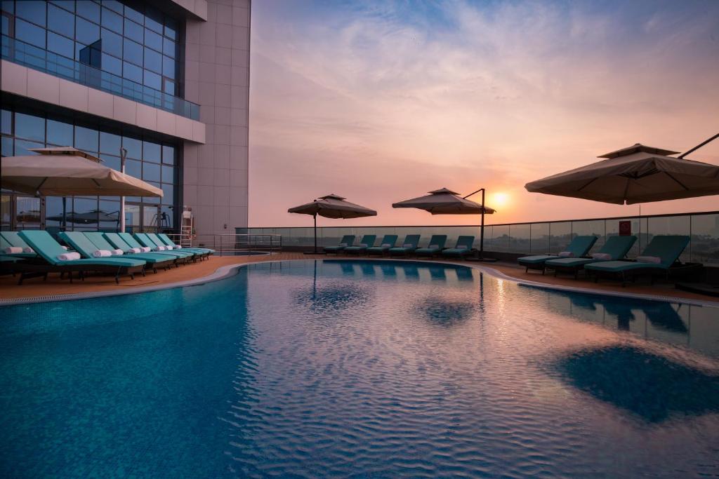 a swimming pool with chairs and umbrellas on a building at Millennium Place Barsha Heights Hotel in Dubai