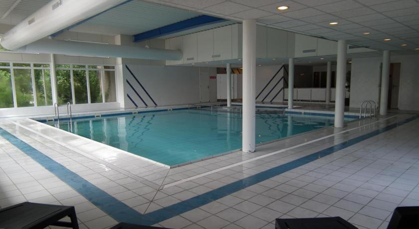 a large swimming pool with blue water in a building at Appartement ZEEDUIN, met VERWARMD ZWEMBAD, eigen KEUKEN, ZONNIG TERRAS nabij DORP, DUINEN en STRAND in Hollum