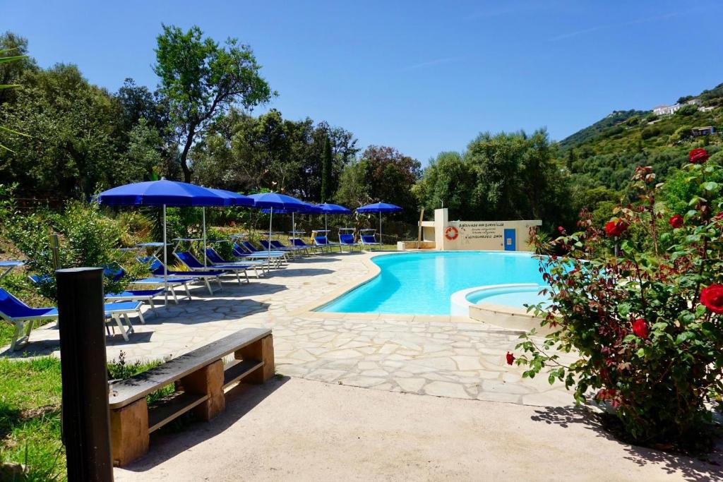 a swimming pool with blue umbrellas and lounge chairs at Résidence Itylon in Cargèse