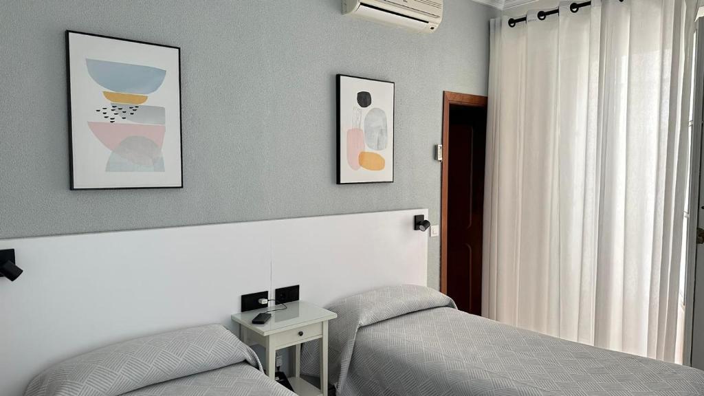 a bedroom with two beds and a table and a window at Hostal Bahía in Cádiz