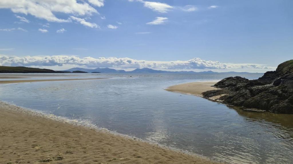 a beach with a body of water and some rocks at 40 Church Street in Aberffraw