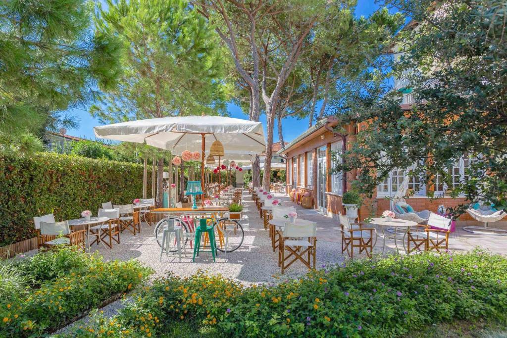 un patio con mesas, sillas y una sombrilla en Hotel La Pineta Al Mare, en Forte dei Marmi