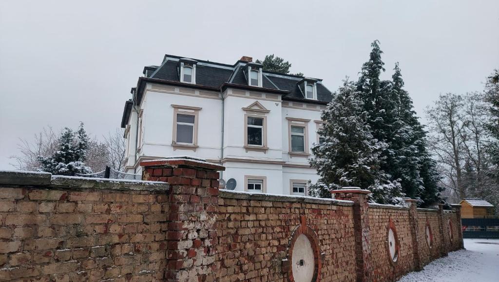 a white house behind a brick wall with snow at Villa Meuselwitz in Meuselwitz