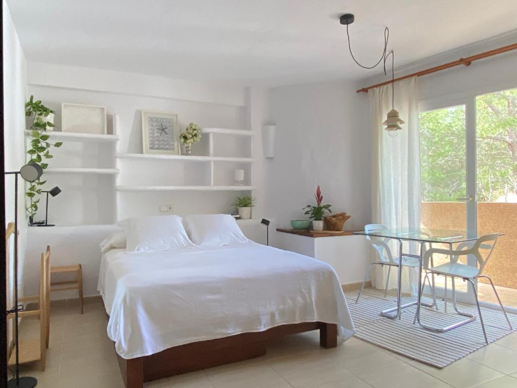 a white bedroom with a bed and a glass table at CALMA Es Pujols in Es Pujols