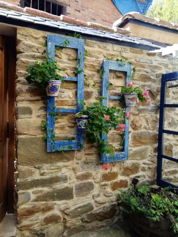 a stone house with blue windows and flowers on it at Casa del patio in Villanueva de Valdueza