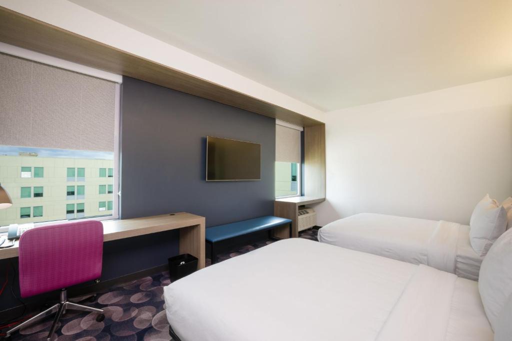 a hotel room with two beds and a desk and a monitor at Aloft Austin Airport in Austin