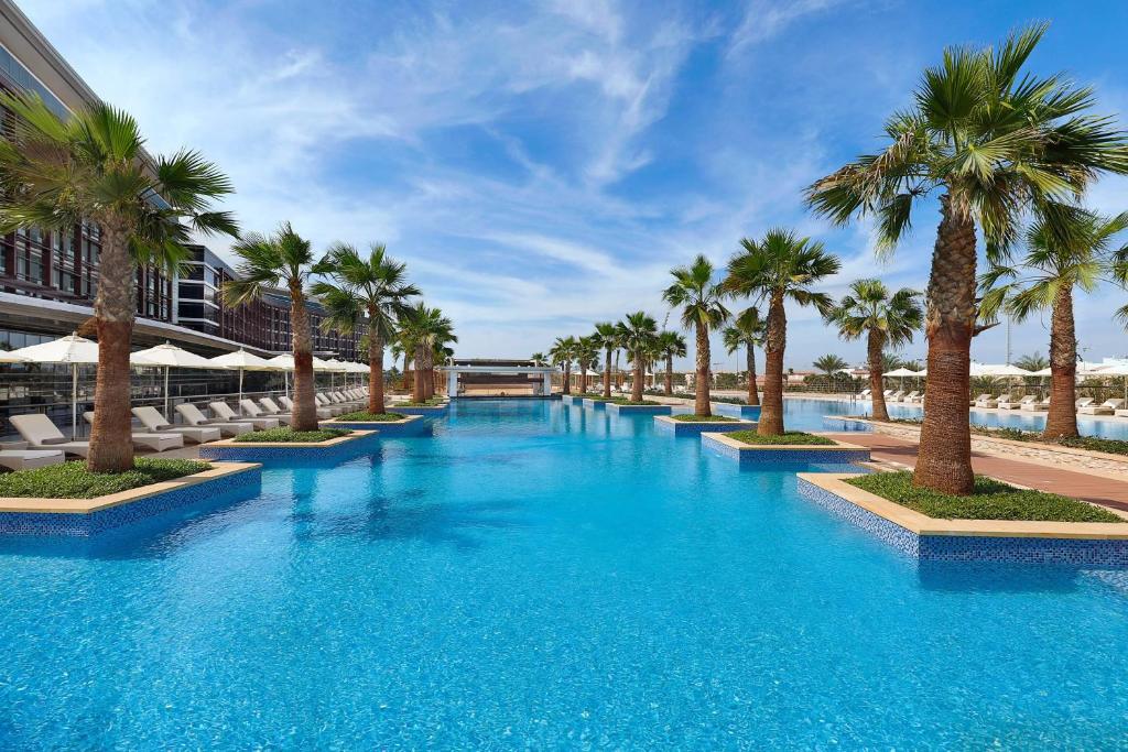 einem großen Pool mit Palmen vor einem Gebäude in der Unterkunft Marriott Hotel Al Forsan, Abu Dhabi in Abu Dhabi