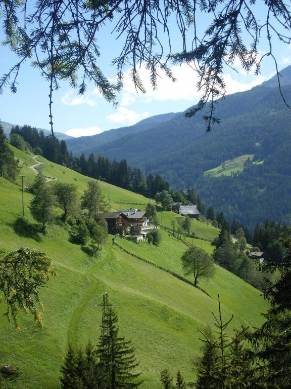 a green hillside with a house in the middle at Unterweg Hof in Sarntal