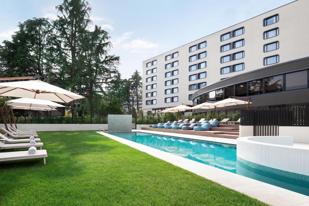 un'immagine di un hotel con piscina, sedie e ombrelloni di Sheraton Milan San Siro a Milano