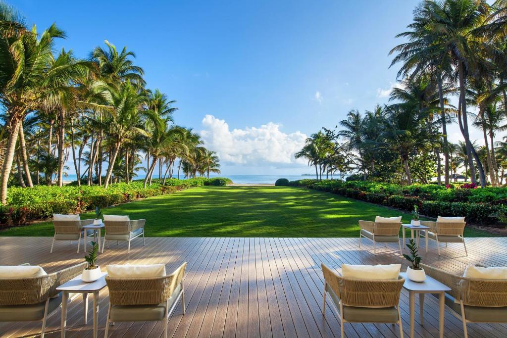 an outdoor patio with chairs and a lawn with palm trees at St. Regis Bahia Beach Resort, Puerto Rico in Rio Grande