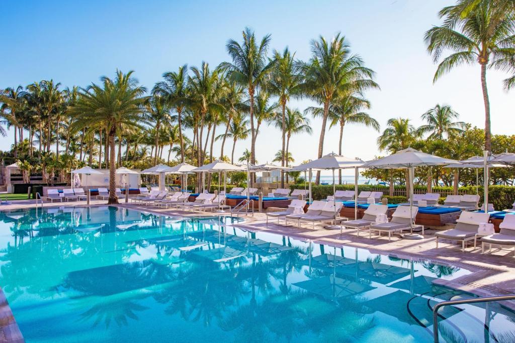 a swimming pool with lounge chairs and palm trees at The St. Regis Bal Harbour Resort in Miami Beach