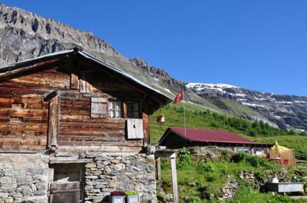 Cabaña de madera con bandera frente a una montaña en Zimmer in uriger rustikalen Alphütte auf bewirtschafteter Alp hoch in den Bergen, inkl VP en Leukerbad
