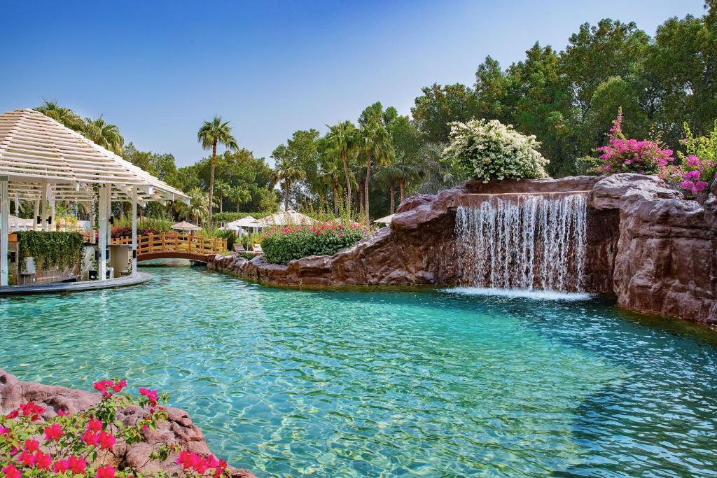 a pool with a waterfall in a yard with flowers at The Ritz-Carlton, Doha in Doha