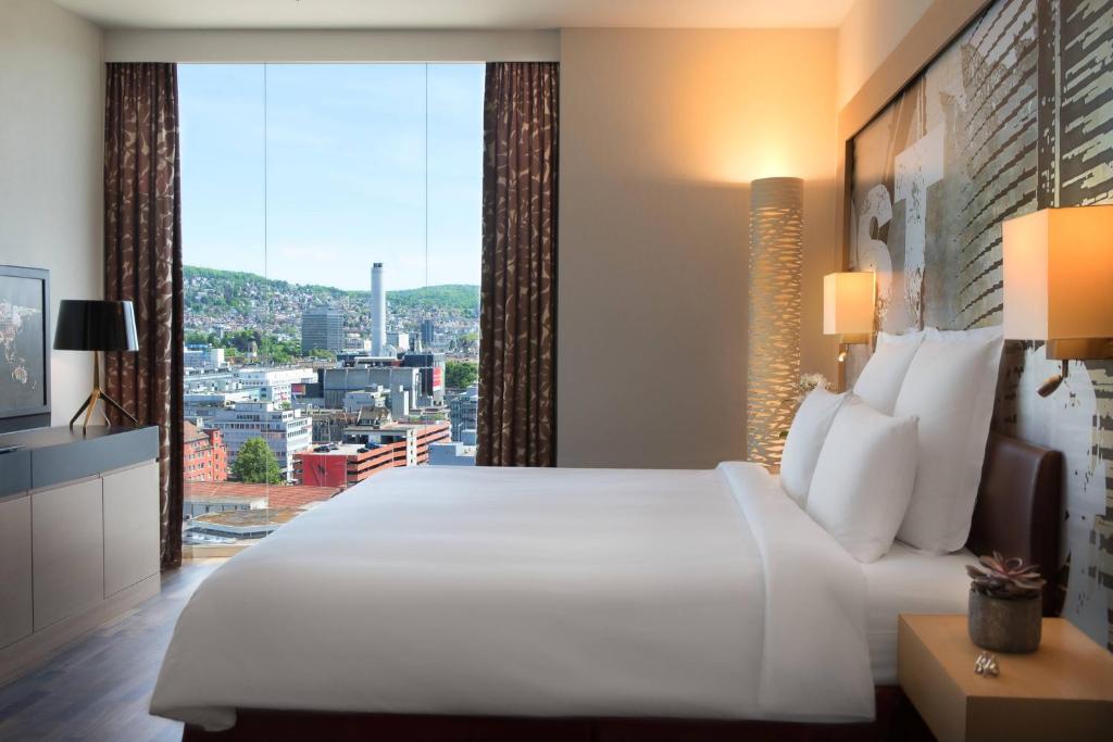 Cette chambre comprend un grand lit blanc et une grande fenêtre. dans l'établissement Renaissance Zurich Tower Hotel, à Zurich