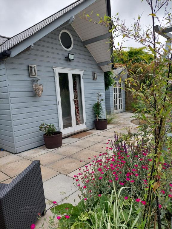 a house with a patio and flowers in front of it at Private Garden Lodge in Christchurch, Dorset for 4 - dogs welcome! in Holdenhurst