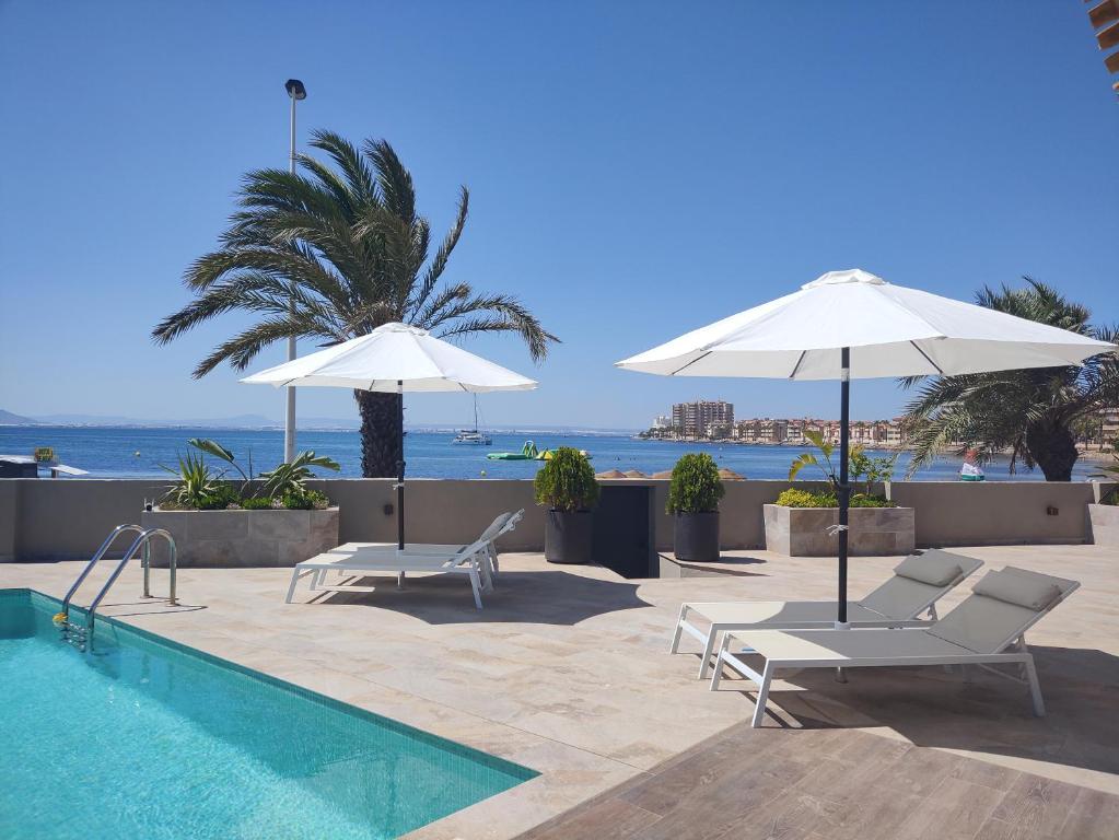 a pool with two umbrellas and two chairs and a palm tree at Boutique Hotel Colina del Emperador in La Manga del Mar Menor