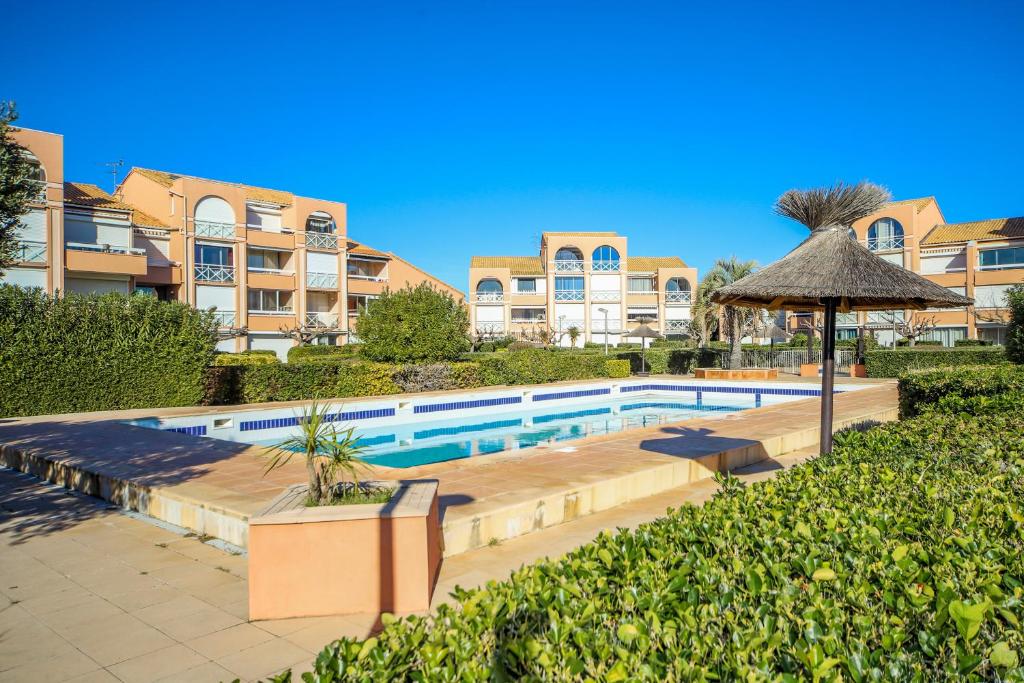 uma piscina com um guarda-sol e alguns edifícios em Le Sénérité Piscine Proche Plage Palavas em Palavas-les-Flots