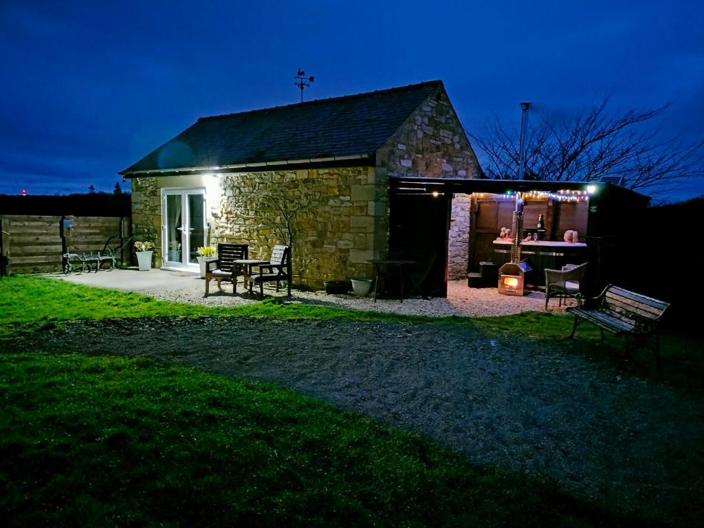 un edificio de piedra con patio por la noche en The Hideaway with hot tub en Chathill