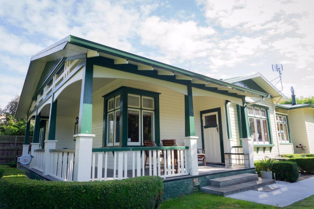 una pequeña casa amarilla y verde con porche en Gumnut House. en Whanganui