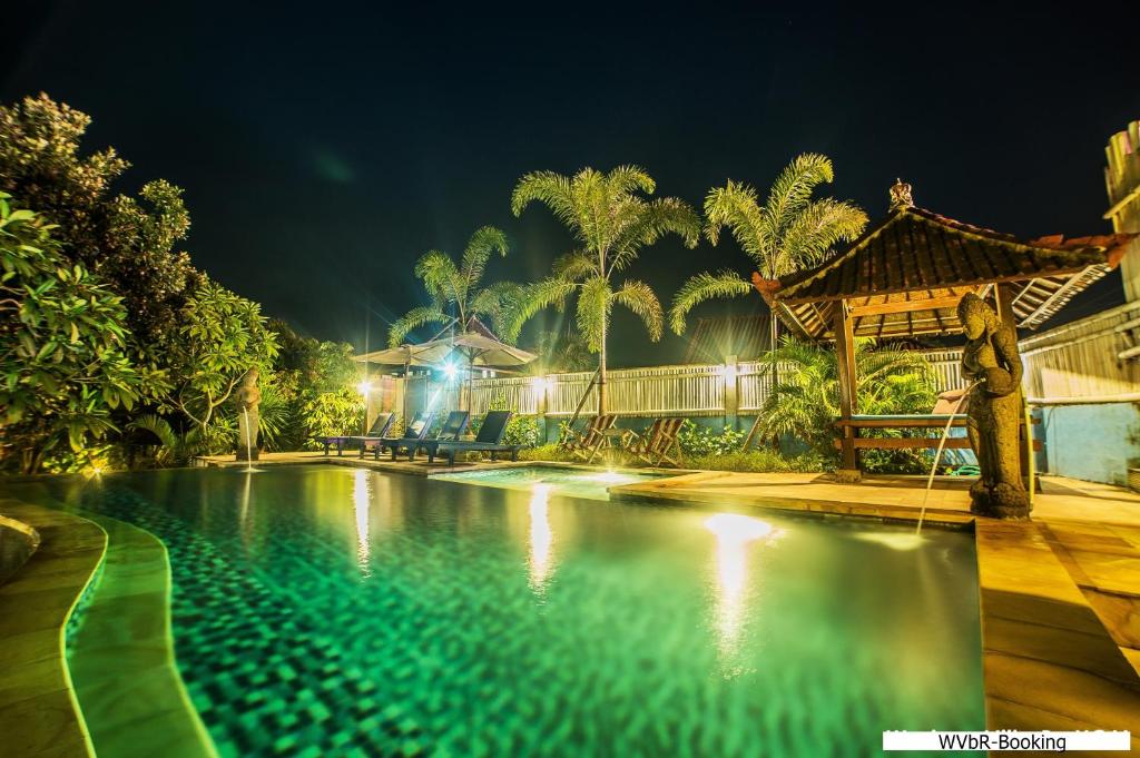 a man standing next to a swimming pool at night at Warisan Villa By Reccoma in Nusa Lembongan