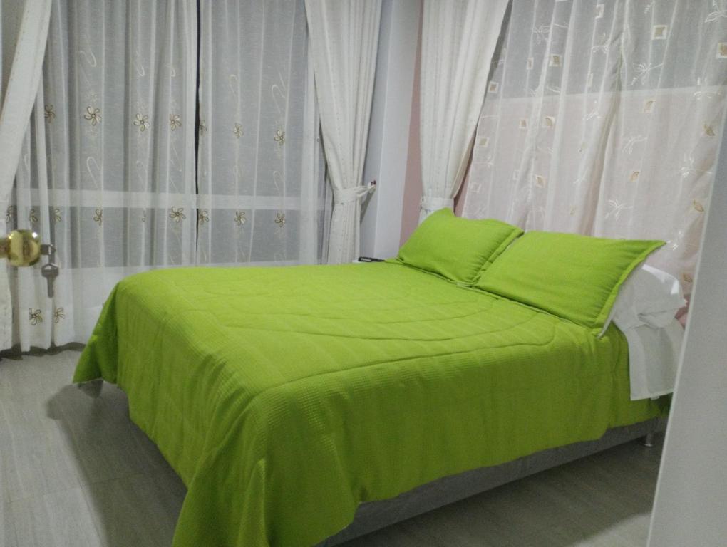 Cama verde en habitación con ventanas en Refugio Flores de María, en Duitama