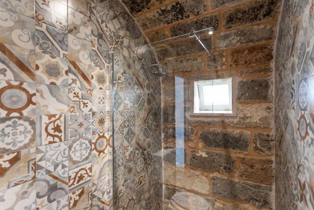 baño con pared de piedra y ventana en MariGiò Rooms, en Alliste