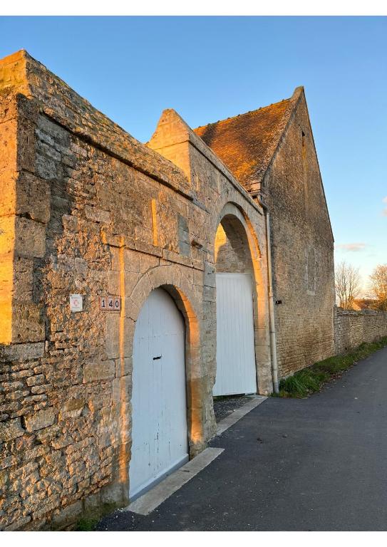 an old brick building with two white garage doors at Les Granges Pelloquin in Bernières-sur-Mer