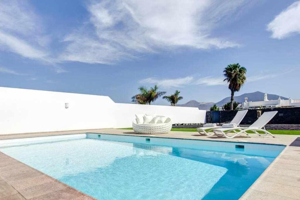 una piscina con 2 sillas blancas en Homu Bianca Fantástica villa con piscina privada, en Playa Blanca