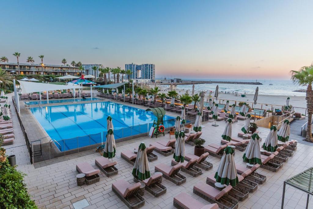 فندق دان أكاديا هرتسليا في هرتسليا: مسبح وكراسي ومظلات بجانب الشاطئ