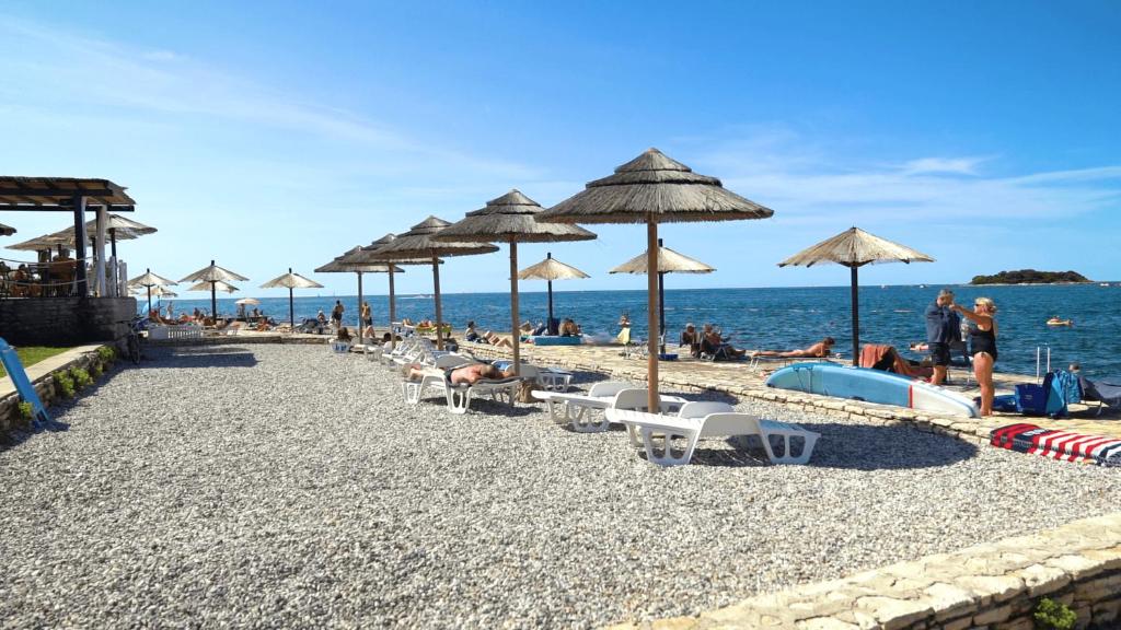 einen Strand mit Stühlen und Sonnenschirmen und Menschen darauf in der Unterkunft Easyatent Mobile home Zelena Laguna in Poreč