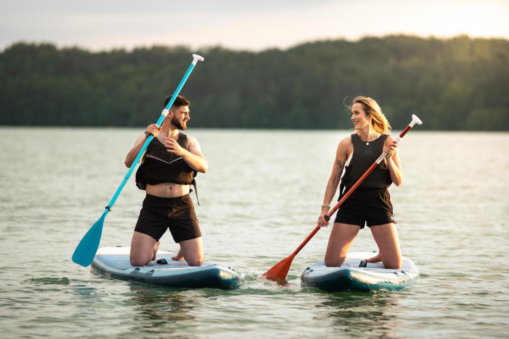 Two people kneeling on paddleboards, paddling on a calm lake with distant treeline