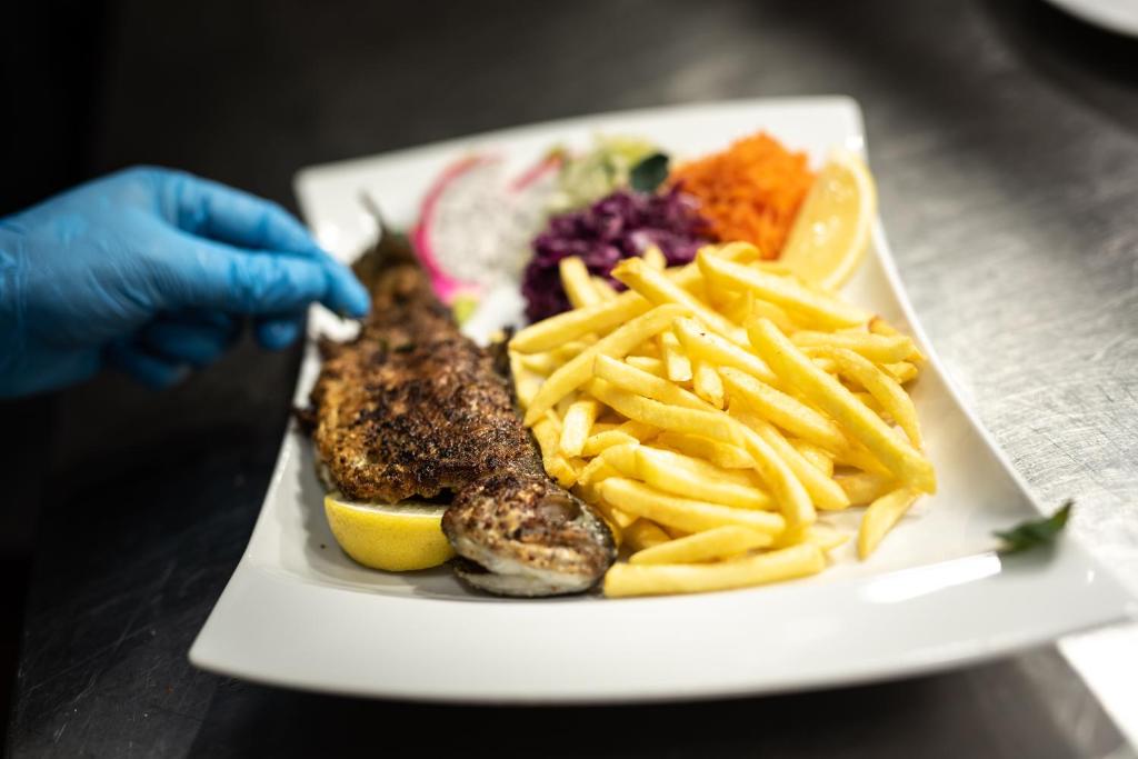 Plated grilled fish with lemon and french fries, chef's gloved hand arranging garnish.