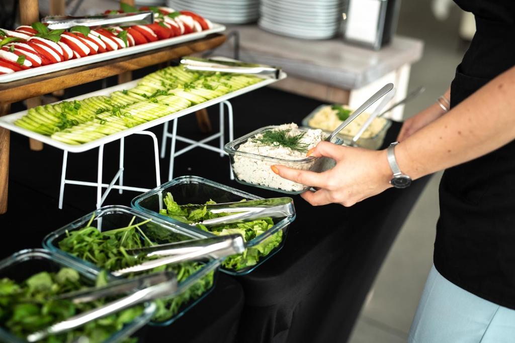 Buffet salad station with sliced cucumbers, mixed greens and server scooping herb spread.