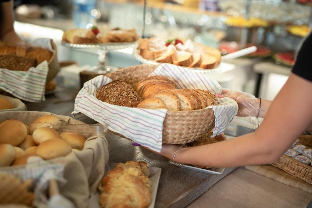 Person holding woven basket of assorted bread rolls at buffet or bakery counter.