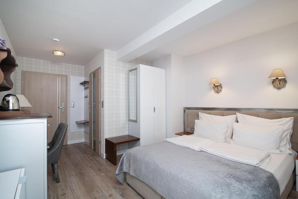 Compact hotel room with double bed, wardrobe, desk and entryway, pale neutral decor.