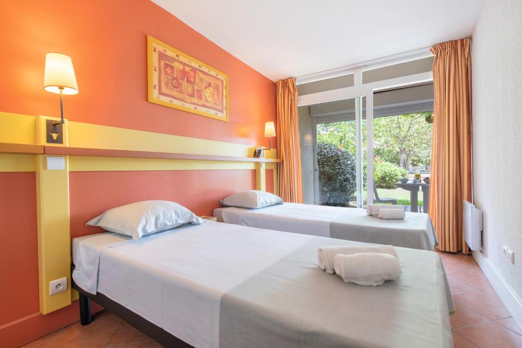 two beds in a room with orange walls and a window at SOWELL RESIDENCES Les Sablons in Le Grau-du-Roi